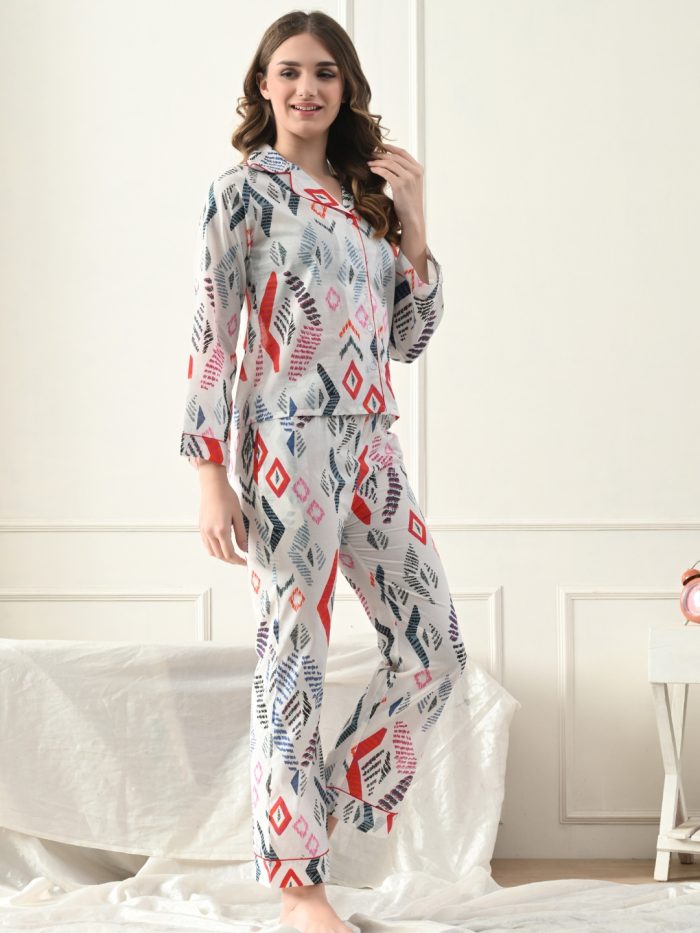 A woman standing in a bedroom wearing a long-sleeved white nightgown with a multicolor geometric print.
